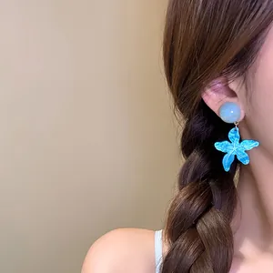 Dettaglio di orecchini a pendente a stella marina blu indossati da una modella