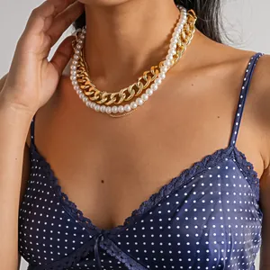 Nahaufnahme einer mehrlagigen Kette mit klobigen Goldketten und weißen Perlen.