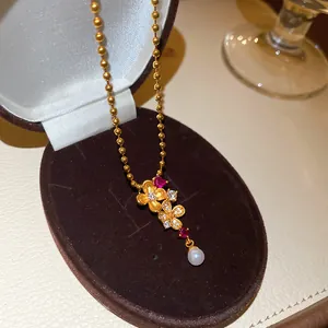 Primer plano del colgante de flor bañado en oro de 24k con circón rojo y perla elegante