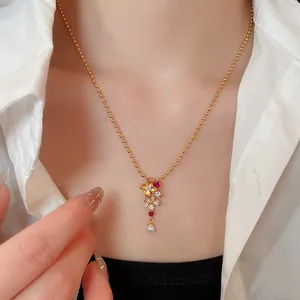 Detalle de collar con colgante de flor dorada con circón rojo y perla colgante fina