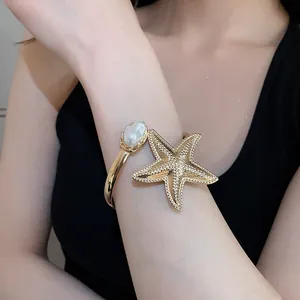 Detailansicht eines goldenen Seestern-Armreifs mit einer eleganten Kunstperle