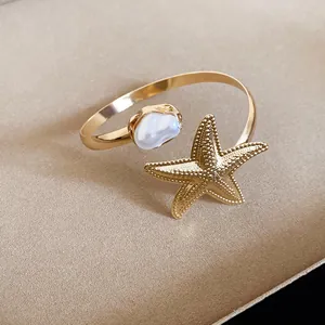 Exquisite Nahaufnahme eines goldenen Armreifs mit Seestern und Perle, verstellbar