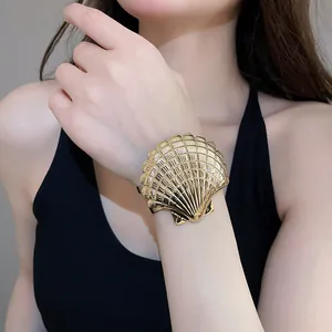 Detaillierte Nahaufnahme eines goldenen Armreifs in Muschelform am Handgelenk eines Modells