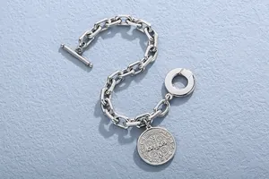 Close-up detail of retro stainless steel link chain bracelet with embossed medallion charm