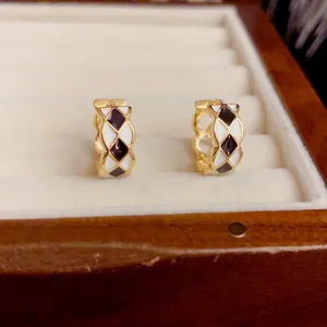 Close-up of gold huggie earrings with black and white checkered enamel diamond pattern