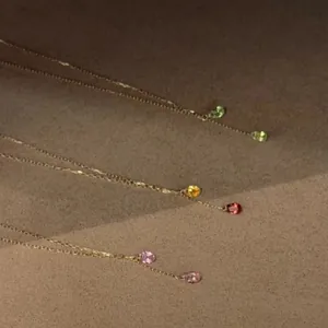 Détail de colliers dorés avec oxydes de zirconium en forme de goutte verts et roses