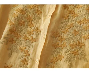 Detail of floral embroidery and pearl buttons on a yellow cotton linen summer shirt