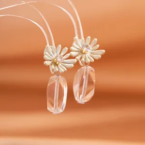 Daisy flower earrings with sparkling crystal pendant on warm orange fabric background