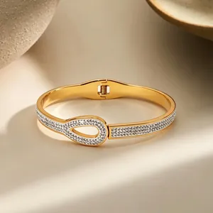Elegant gold-tone stainless steel bangle featuring teardrop clasp and pavé rhinestones