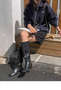 Close-up of black knee-high boots with square toe and side zipper on wooden stairs