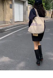 Street style view of cream canvas tote bag with purple graphics and black tall leather boots