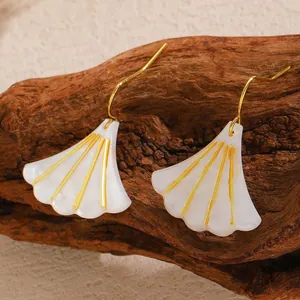 Detailed view of ginkgo leaf earrings with shell texture and golden trim on wood