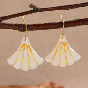 Close-up of elegant ginkgo leaf earrings with gold accents on a natural wood branch