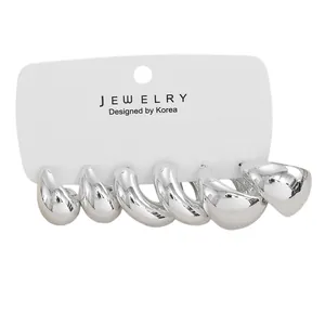 Macro shot of three pairs of silver-colored thick C-shape hoop earrings on a display card