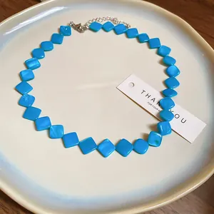 Elegante Edelstahl-Halskette mit blauen Rautenperlen auf einem weißen Keramikteller