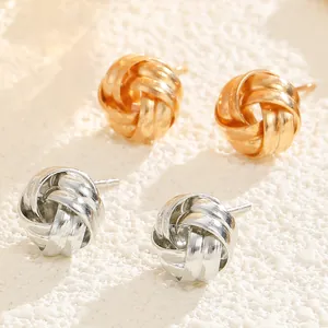 Detail of twisted knot stud earrings in gold and silver finish on stone surface