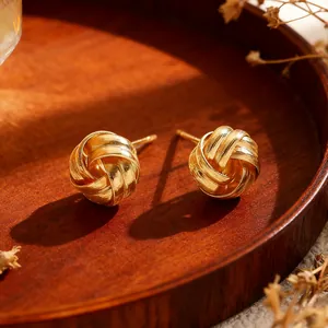 Detailed view of golden twisted knot stud earrings on a wooden tray with warm sunlight