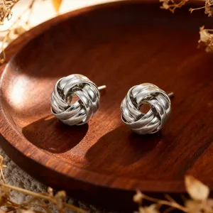 Macro shot of silver woven knot earrings on a rustic wood tray with elegant details