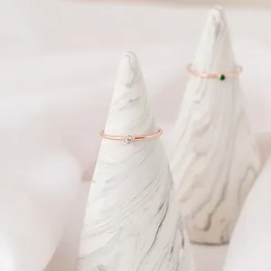 Macro detail of rose gold slim rings featuring white zircon and green gemstone on white cones