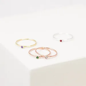 Close-up of four minimalist thin band rings with multi-color gemstones on white blocks