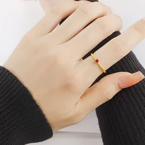 Elegant minimalist gold band ring with a tiny red gemstone on hand with black cuff