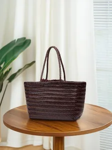 Handwoven dark brown leather tote bag with dual handles on a wooden table setup
