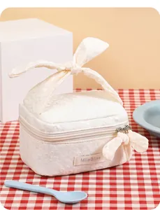 Detail of white lace makeup bag featuring a large bow handle and floral embroidery