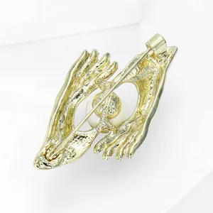 Elegant gold-tone hands holding a white pearl creative brooch pin for suit accessories