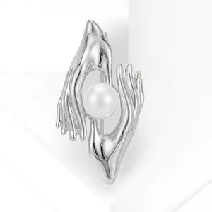 Close-up of a creative silver-toned brooch with a unique hands holding pearl design.