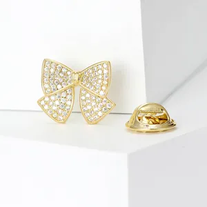 Macro detail of a gold-plated bow brooch with sparkling cubic zirconia on a white pedestal