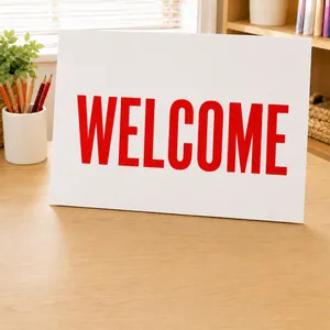 Close-up of white Welcome sign with bold red lettering on a natural wooden desk