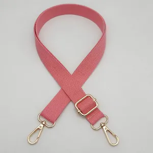 Détail d'une bandoulière rose ajustable en toile tissée avec mousquetons en métal doré