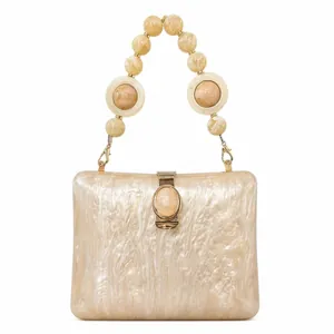 Detail of creamy white acrylic box clutch with pearl texture and gold hardware clasp