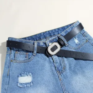 Dettaglio di una cintura nera con fibbia di perle abbinata a jeans in denim blu chiaro