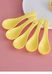 Detailed view of five yellow matte ceramic spoons with hanging holes on a pink background