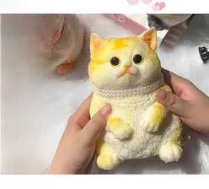 Close-up of yellow calico cat squishy toy with pearl necklace being squeezed by hand