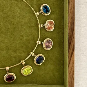 Detail of colorful oval birthstone pendants in gold bezel setting on a green velvet surface
