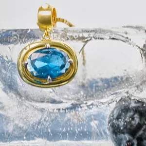Macro detail of oval blue gemstone pendant with gold bezel set on ice and blueberries