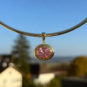 Close-up of an oval pink zircon pendant with gold plated base against a sky background