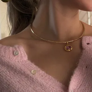 Close-up of a gold metal choker necklace featuring a round pink birthstone zircon pendant