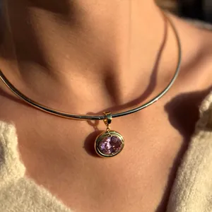 Close-up of an oval pink zircon pendant on a gold torque necklace worn by a model