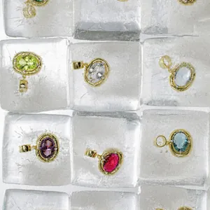 Macro view of multi-color oval gemstone pendants with gold frames on ice cubes