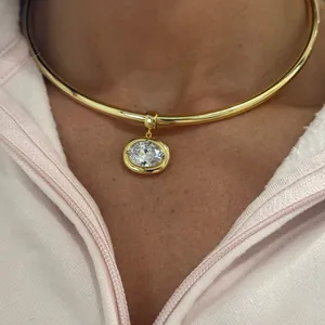 Close-up of a large oval birthstone pendant on a gold collar necklace worn by a person