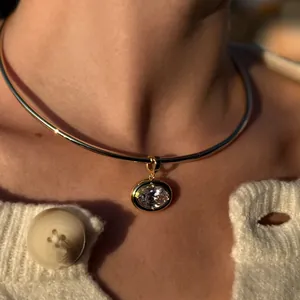 Close-up of a gold choker with an oval crystal pendant worn on a model with white knitwear