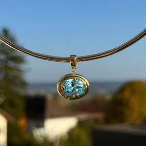Detailed close-up of an oval light blue gemstone pendant in a gold-plated bezel setting