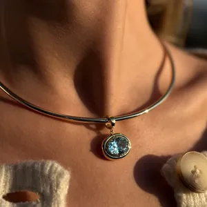 Close-up of gold choker with oval light blue gemstone pendant worn by a model