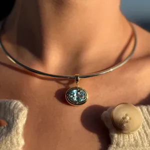 Light blue oval gemstone pendant on a gold metal collar necklace worn by a model
