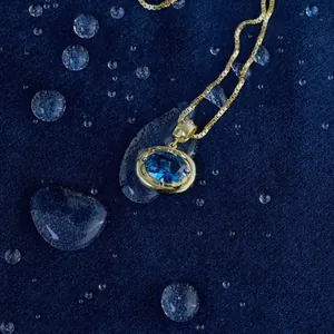 Detail of gold box chain necklace with oval blue gemstone pendant and water drops