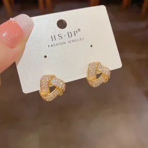Macro detail of gold knot earrings with micro-pave crystals on a white display card