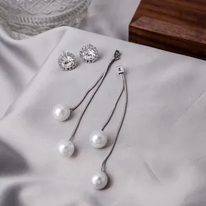 Close-up of sparkling zircon stud earrings and long silver tassel pearl drop earrings